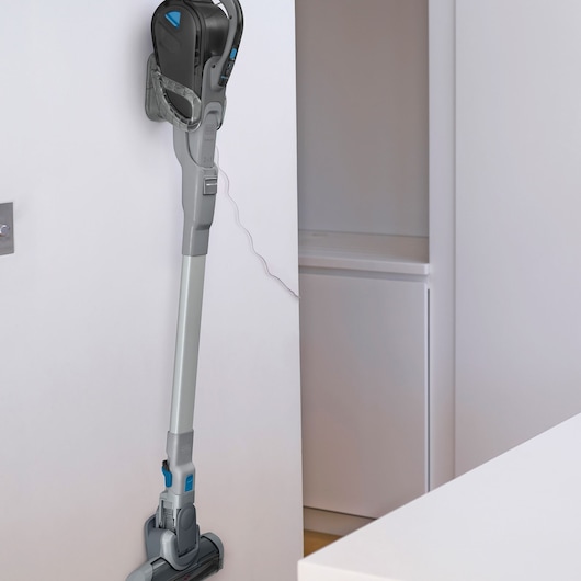 BLACKDECKER cordless stick vacuum FEJ520JF mounted on a white wall, side angle, charging in a modern room.