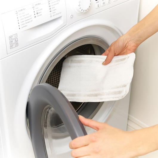 BLACKDECKER FSM1605 steam mop pad being placed into front-load washing machine, close-up view.
