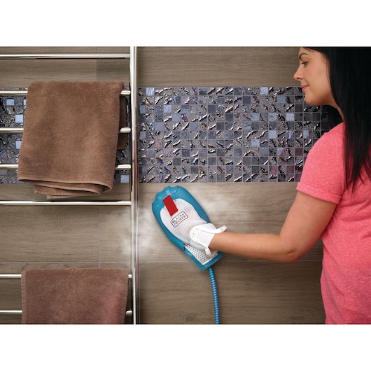 BLACK+DECKER FSMH13101SM handheld steam cleaner in use, cleaning mosaic tile wall near towel rack.