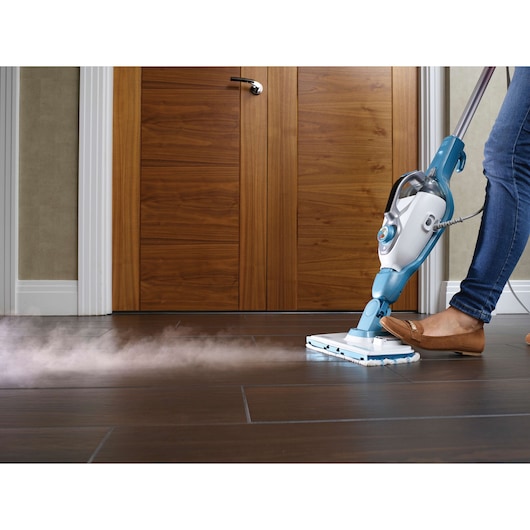 Photo of BLACKDECKER FSMH13101SM steam mop cleaning dark wood floor, person pressing pedal, front angle.