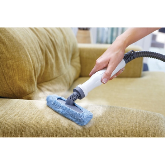 BLACKDECKER FSMH13151SM handheld steam cleaner with blue microfiber pad cleaning yellow fabric sofa, close-up.