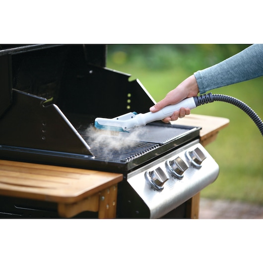BLACKDECKER FSMH13151SM steam cleaner cleaning a barbecue grill with steam outdoors, product in use.