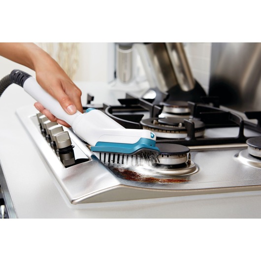 BLACKDECKER FSMH13151SM steam cleaner brush scrubbing a stainless steel stove top, close-up view.