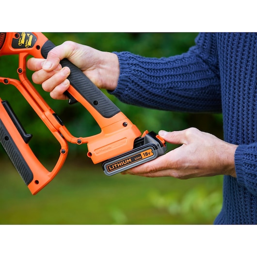 A person is holding an orange and black BLACK+DECKER cordless tool, focusing on the handle and the detachable 18V lithium battery.