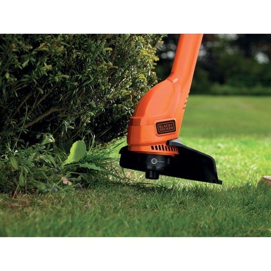 BLACK+DECKER GL250 orange grass trimmer in use near shrubbery on lawn.