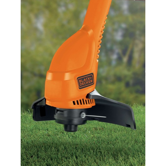 Close-up view of a BLACK+DECKER orange grass trimmer cutting green grass outdoors.