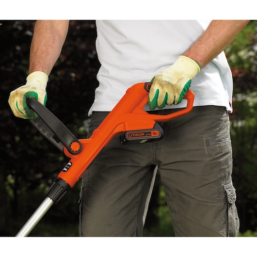 Photo of BLACKDECKER GLC1823L20 orange cordless grass trimmer being held by a person wearing garden gloves.