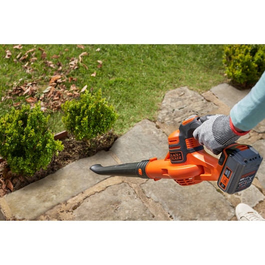 BLACK+DECKER GWC1820PC cordless leaf blower being used on a stone path near shrubs.