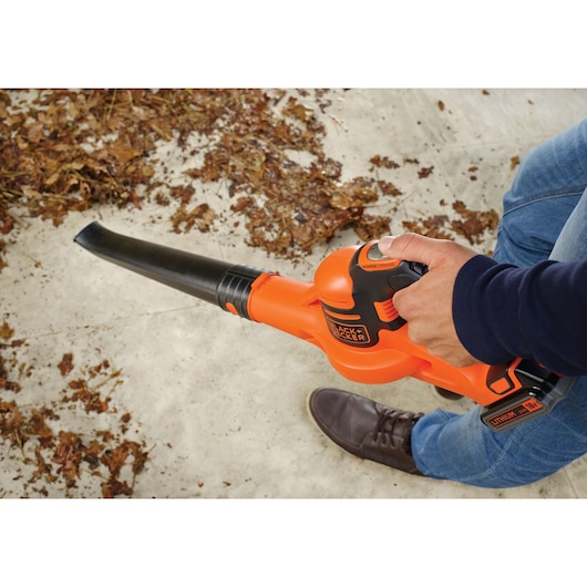 BLACK+DECKER GWC1820PC cordless leaf blower in use, orange and black design, blowing leaves on pavement.