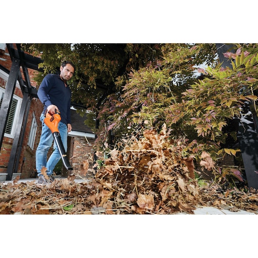 BLACKDECKER GWC1820PC cordless leaf blower in use, clearing dry leaves on a patio.