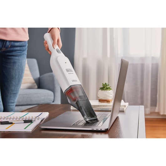 BLACKDECKER HLVC315B11 handheld vacuum cleaning a laptop keyboard on a desk in a living room.