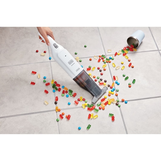 Photo of BLACK+DECKER HLVC315B11 handheld vacuum cleaning colorful candy from tiled floor, top view.