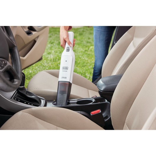 BLACKDECKER HLVC315J11 handheld vacuum cleaning car interior between beige seats.