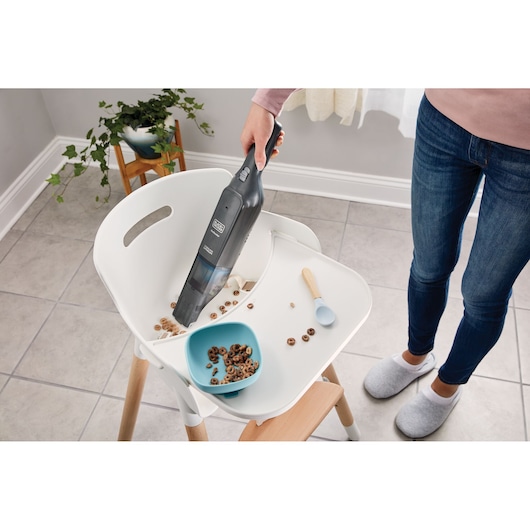 BLACKDECKER HLVC320B11 handheld vacuum cleaning cereal from white high chair tray, home setting.