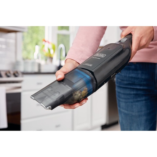 BLACK+DECKER HLVC320B11 handheld vacuum in use, picking up debris in a kitchen.