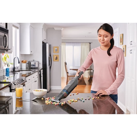 BLACKDECKER HLVC320J11 handheld vacuum cleaning cereal on kitchen counter.
