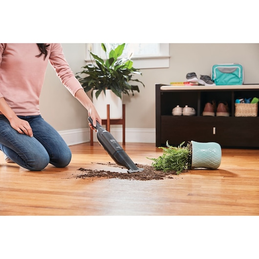 BLACKDECKER HLVC320J11 handheld vacuum cleaning spilled soil on hardwood floor in a home setting.