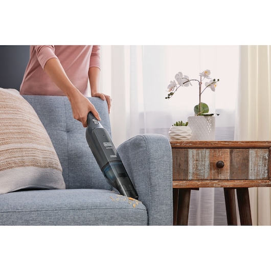 Photo of BLACK+DECKER HLVC320J11 handheld vacuum cleaning crumbs from a blue sofa next to a wooden side table.