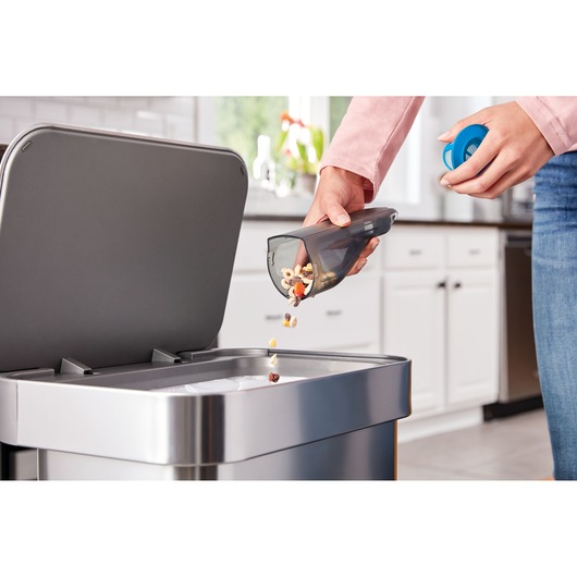 BLACK+DECKER HLVC320J11 vacuum dustbin being emptied into a kitchen trash can, close-up view.