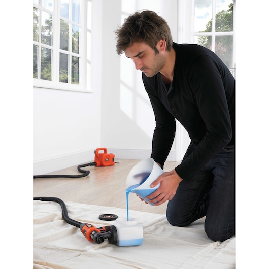 BLACKDECKER HVLP400 paint sprayer on floor with blue paint being poured into container indoors.