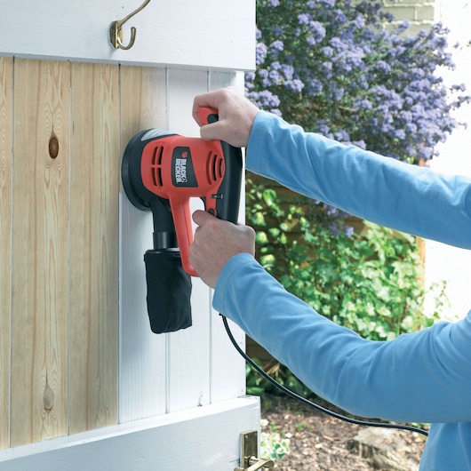 BLACKDECKER KA191EK sander in use on wooden door panel outdoors.