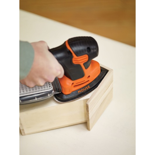 A person is using a BLACK+DECKER KA2500K Mouse sander to smooth the surface of a wooden box corner.
