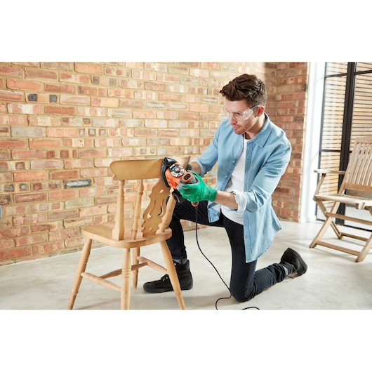 Photography of BLACKDECKER KA280LSA2 multi sander used to sand a wooden chair indoors.