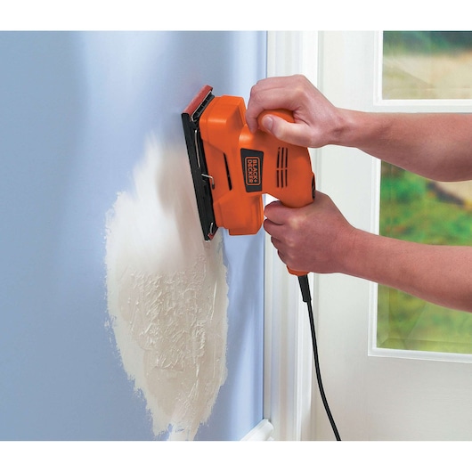 Photo of BLACKDECKER KA300 orange electric sander smoothing plaster on blue wall.