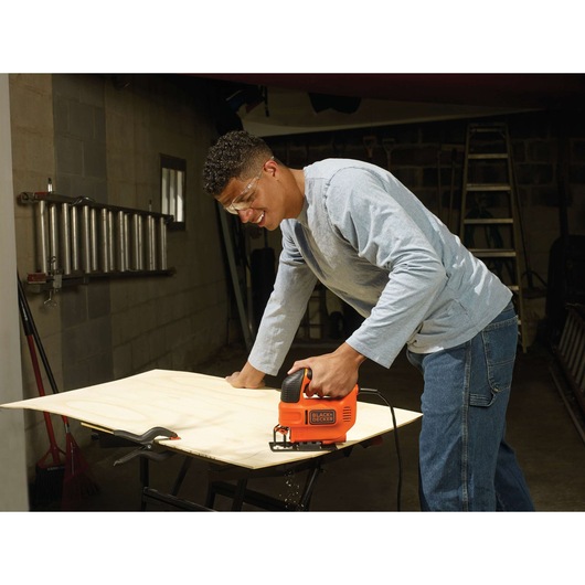 Photo of BLACKDECKER KS701E jigsaw cutting plywood on a workbench in a workshop.