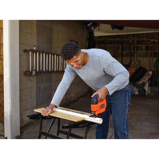 Photography of BLACKDECKER KS701E jigsaw cutting a white PVC pipe on a workbench in a garage.