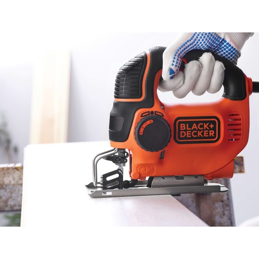 Photo of BLACK+DECKER KS901PEK orange jigsaw tool being used to cut wood, product category photography.