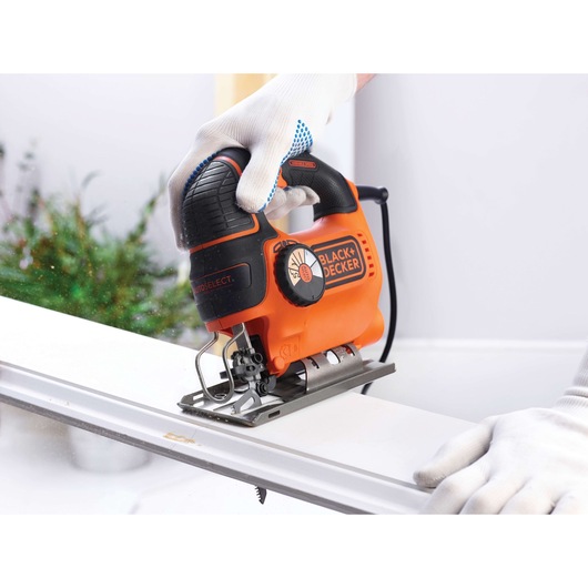 Photo of BLACK+DECKER KS901SEK orange and black jigsaw being used to cut a white board, close-up view.