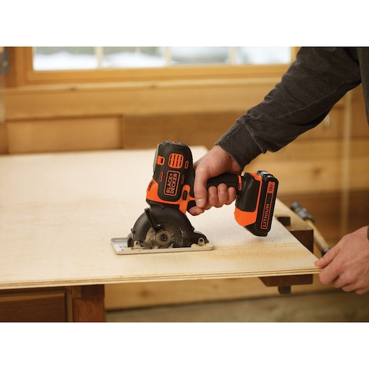 BLACKDECKER MT218K cordless mini circular saw cutting wood in workshop, close-up of tool in use.