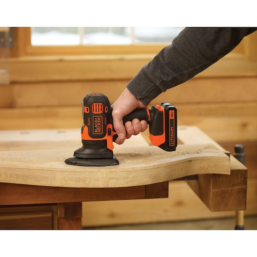 BLACK+DECKER MT218K cordless sander in use on wood, black and orange colors, close-up side angle.