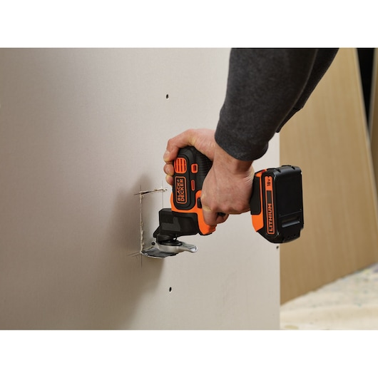Photo of BLACKDECKER MT218K cordless oscillating tool cutting drywall, visible hand operation.