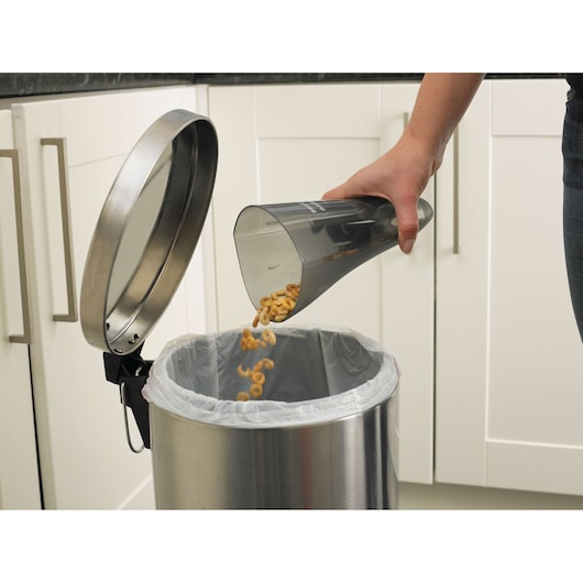 BLACKDECKER NV3610N handheld vacuum dustbin being emptied into kitchen trash can, close-up side angle.