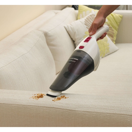 BLACKDECKER NV3620N handheld vacuum cleaning crumbs on a light sofa, with pillows in background.
