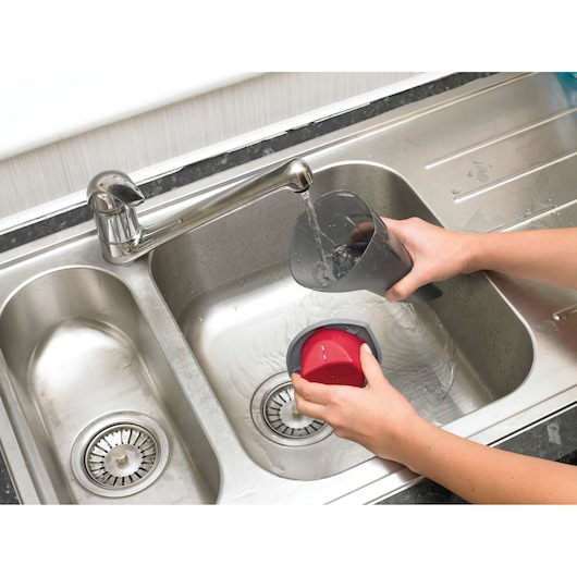 Photo of BLACKDECKER NV3620N vacuum dust container being cleaned under running water in a kitchen sink.