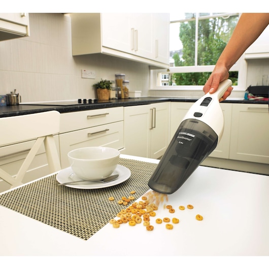 BLACKDECKER NV4820N handheld vacuum cleaner picking up cereal from kitchen table, side angle.