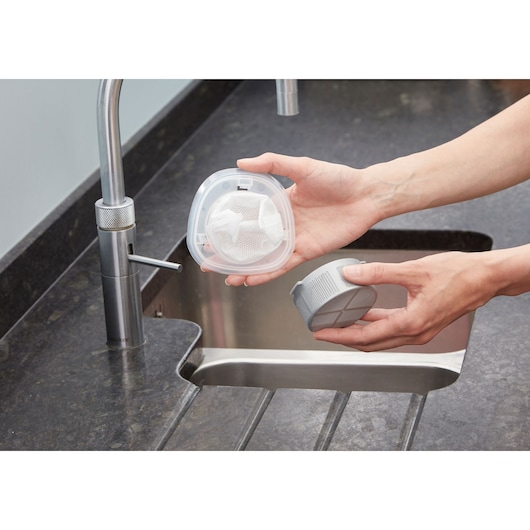 A person holding two removable filter parts over a kitchen sink, with a faucet visible in the background.
