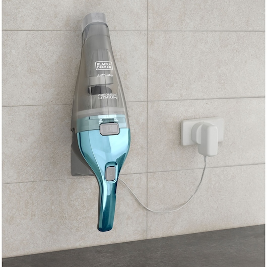 A BLACK+DECKER cordless lithium handheld vacuum cleaner mounted on a wall and connected to a power outlet for charging.