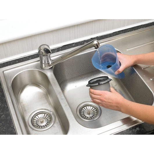 BLACKDECKER NW3620N vacuum filter being rinsed under a kitchen faucet, closeup of hands and stainless steel sink.