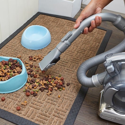 BLACKDECKER PD1820L handheld vacuum cleaning pet food from mat, flexible hose, close-up angle.