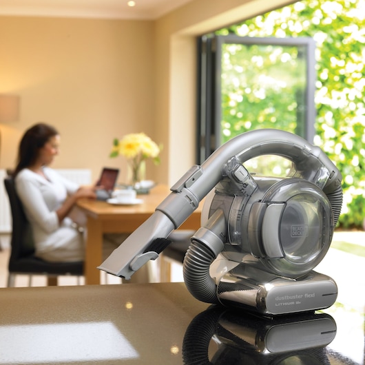 BLACKDECKER PD1820L dustbuster flexi lithium vacuum cleaner on countertop, bright home setting, woman blurred in background.