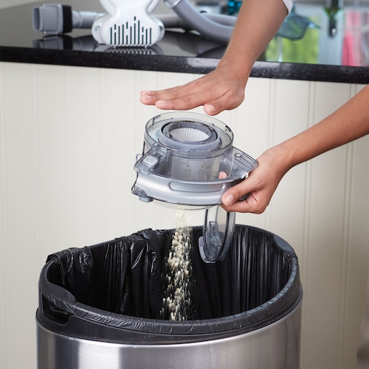 BLACKDECKER PD1820L vacuum dust container being emptied over a trash bin, close-up view.