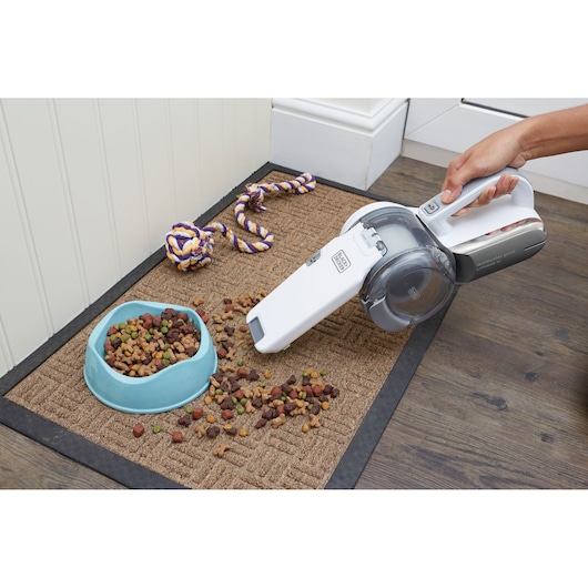BLACKDECKER PV1820L handheld vacuum cleaning spilled pet food on brown mat next to blue bowl.