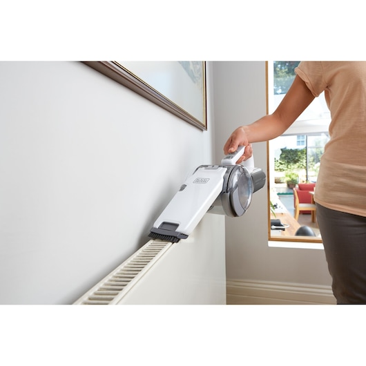 BLACK+DECKER PV1820L handheld vacuum cleaning a radiator with a brush attachment in a home setting.