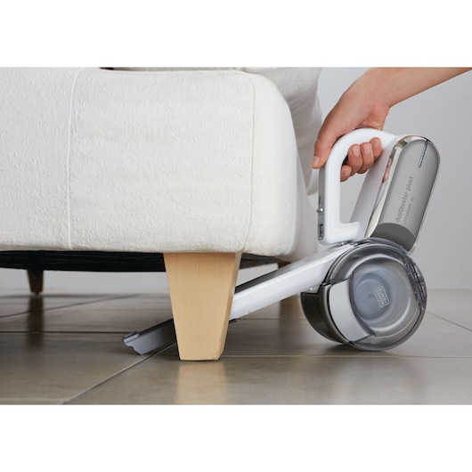 BLACKDECKER PV1820L handheld vacuum cleaning under sofa, angled side view.