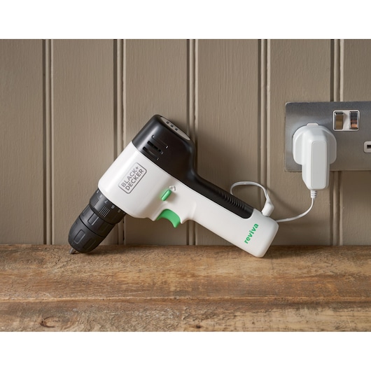 Photo of BLACK+DECKER REVDD12C cordless drill in black and white, charging on a wooden surface near a wall socket.