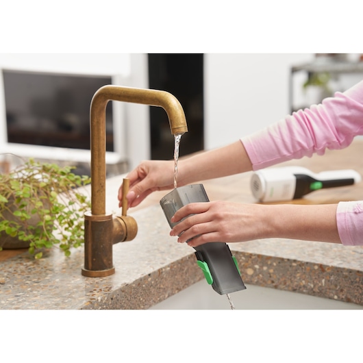 BLACKDECKER REVHV8C handheld vacuum filter being rinsed under kitchen faucet, countertop view.